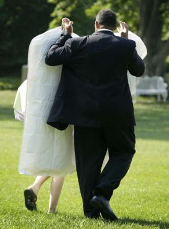A White House valet holds a pair of garment bags over Jenna Bush, daughter of U.S. President George W. Bush, as she makes her way to Marine One on the South Lawn of the White House July 5, 2002. White House personnel appeared to be trying to shield the president's daughter from members of the White House Press Corps, again. Photo by Win McNamee