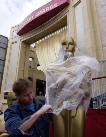 Terry O'Toole pulls a plastic bag over a large Oscar statue to protect it from the rain as preparations continue, Saturday, March 23, 2002 in Los Angeles for the Academy Awards. Photo by Laura Rauch