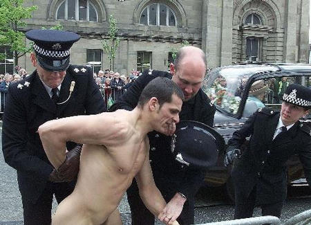 Britain's Queen Elizabeth II, right background, is driven past, as police officers restrain a streaker in Newcastle, England, Tuesday May 7, 2002. Photo by Owen Humphreys